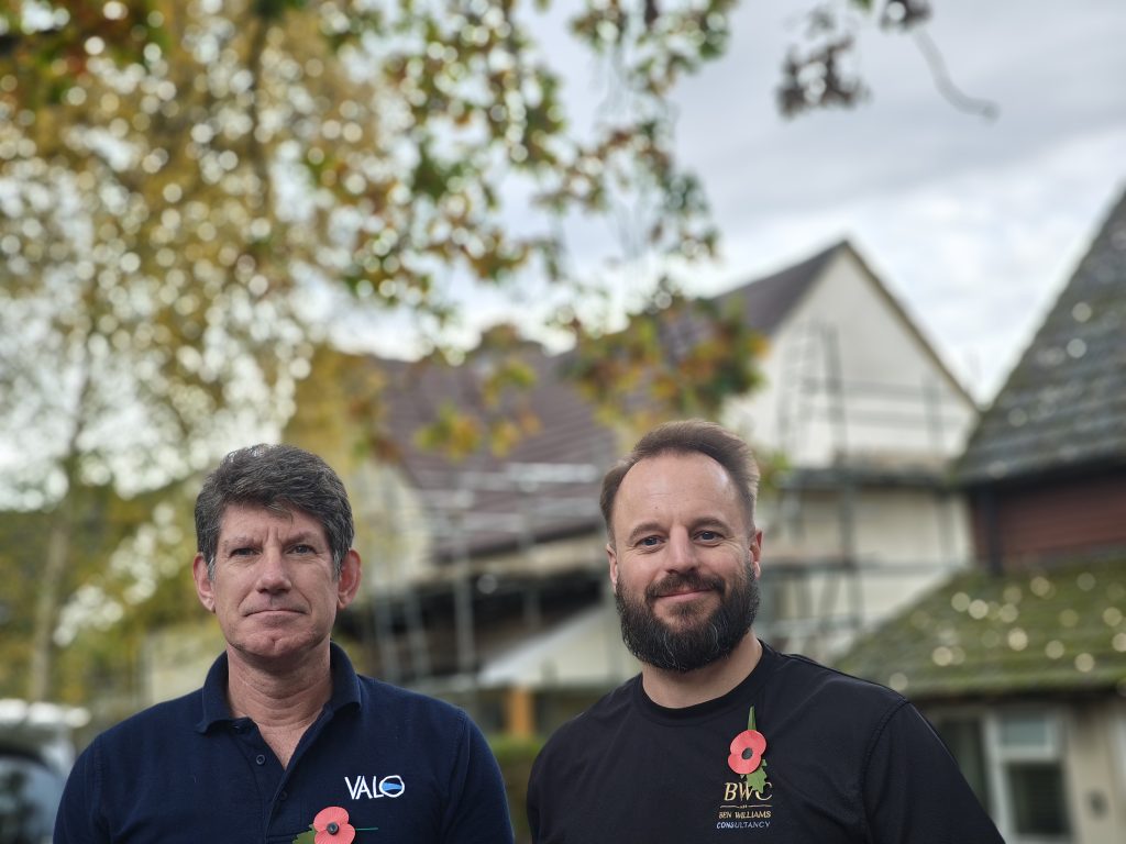 two men with poppies smiling infront of a house one with a black top beard and BWC logo one with blue top and VAL on his top. 